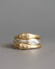 Three stacked rings featuring stylized human face profiles, with two in polished yellow gold and one in silver, set against a soft gray background.