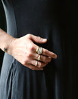 A close-up of a person's hand wearing multiple gold rings, including one with a marquise-cut gemstone and others with textured bands, set against a dark black dress.