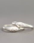 A pair of silver rings shaped like stylized faces, resting on a neutral gray surface.