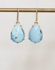 Pair of turquoise teardrop earrings on a gold hook against a light gray background