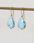 Turquoise teardrop earrings on a gold hook against a light gray background