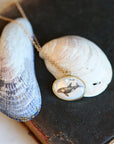 Necklace with a whale pendant on a dark surface with shells