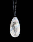 Teardrop-shaped pendant with mermaid design on a black background