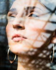 large gold hoops shown on person, shown through a window with reflection