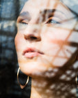 large gold hoops shown on person, shown through a window with reflection