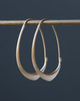 small gold facet hoops hanging from a bar against a grey background
