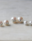 Three pairs of pearl studs in a row, photographed on white marble. From left to right, the medium pearl studs with silver barnacles, the large pearl studs with silver barnacles, and the little pearl studs with silver barnacles.