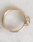A gold ring with a small cluster of clear gemstones and a tiny blue accent, photographed from above on a light marble surface.