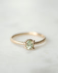 an oval pale aloe green montana sapphire is set in a gold ring within a-symmetrial gold prongs