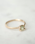 side view of an oval pale aloe green montana sapphire is set in a gold ring within a-symmetrial gold prongs