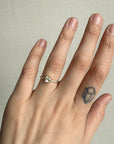 Hand wearing a ring with a small white stone ring on a neutral background
