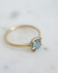 a muted teal round sapphire sits within gold prongs in this gold ring, a hidden halo of diamonds beneath. side view.