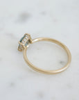 a muted teal round sapphire sits within gold prongs in this gold ring, a hidden halo of diamonds beneath. back view.