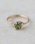a heavily included green garnet round gemstone is set in a gold branch ring with vine-like prongs. Front view.
