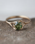 a heavily included green garnet round gemstone is set in a gold branch ring with vine-like prongs. Front view.