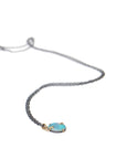 green and blue flash oval opal set in gold branch prongs, on a black chain, on white. by hannah blount