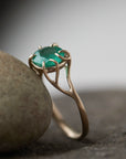 Round green emerald is set in a branch ring with branchy prongs holding the stone. Photographed leaving on a stone. side view.