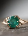 Round green emerald is set in a branch ring with branchy prongs holding the stone. Photographed on stone. Front view.