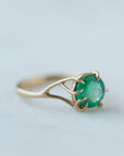 Round green emerald is set in a branch ring with branchy prongs holding the stone. Photographed on stone. Side view.