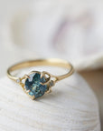 oval teal montana sapphire is set in a gold branch ring with vine-like prongs holding the stone in. Three little diamond berries adorn the branches. Front view.