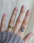 Hand wearing a ring with a green gemstone on a neutral background
