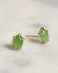 Pair of green jade cabochon stud earrings with five 14k yellow gold prongs on a light background.