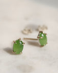 Pair of green jade cabochon stud earrings with five 14k yellow gold prongs on a light background.