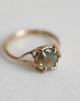 Gold ring with a multicolored gemstone on a light gray background
