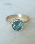 teal montana sapphire set within a bezel of a yellow gold ring, with white gold barnacles and diamonds