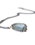 oval cool moss aquamarine sits in gold prongs with black and roses and chain.
