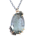 oval cool moss aquamarine sits in gold prongs with black and roses and chain.