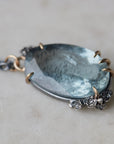 oval cool moss aquamarine sits in gold prongs with black and roses and chain.