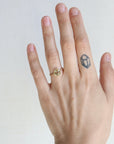 Hand wearing a gold ring with a small diamond-shaped tattoo on the finger against a plain background