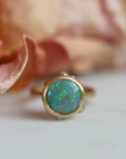 Gold ring with a green gemstone next to a pink flower