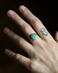 Hand wearing a ring with an opal stone on a dark background