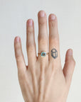 Hand wearing a ring with a blue gemstone on a plain background