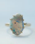 raw opal with rainbow colors is set within eight gold prongs on a gold band. A single diamond sits atop the band next to the opal, like a little friend.