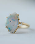 raw opal with rainbow colors is set within eight gold prongs on a gold band. A single diamond sits atop the band next to the opal, like a little friend.