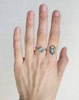 Hand wearing a ring with a blue gemstone on a plain background