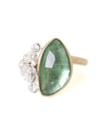 abstract green tourmaline rose cut gemstone set in a gold bezel with a bouquet of silver roses on one side.