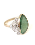 abstract green tourmaline rose cut gemstone set in a gold bezel with a bouquet of silver roses on one side.