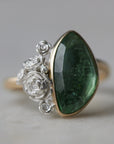 abstract green tourmaline rose cut gemstone set in a gold bezel with a bouquet of silver roses on one side.