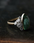 abstract green tourmaline rose cut gemstone set in a gold bezel with a bouquet of silver roses on one side.