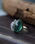 abstract green tourmaline rose cut gemstone set in a gold bezel with a bouquet of silver roses on one side.