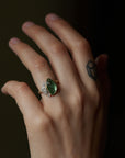 abstract green tourmaline rose cut gemstone set in a gold bezel with a bouquet of silver roses on one side. Shown on person.