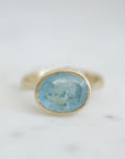 An oblong faceted aquamarine is set in a gold band with little silver barnacles around the setting. Front view.
