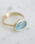 An oblong faceted aquamarine is set in a gold band with little silver barnacles around the setting. 1/4 view.