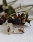 Pair of earrings with leaf design on a white surface with dried leaves in the background