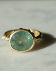 hard natural lighting on a pale teal montana sapphire set in yellow gold ring with barnacles