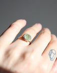 Hand wearing a ring with a green stone on a gray background